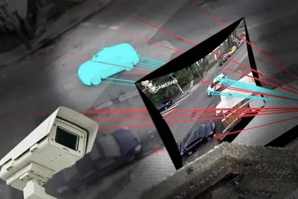 Uma imagem que mostra uma cena de vigilância urbana capturada por uma câmera de segurança. Na parte inferior esquerda, há uma câmera montada em um poste, apontando para uma rua. Na imagem, linhas vermelhas e azuis indicam o rastreamento de movimento, conectando a câmera a um veículo azul destacado na rua abaixo. Um monitor flutuando na parte central da imagem exibe uma visão ampliada da rua, com o mesmo veículo azul sendo rastreado por linhas azuis. A cena ocorre à noite, com iluminação escassa e superfícies escuras, sugerindo uma análise de tráfego ou monitoramento em tempo real.